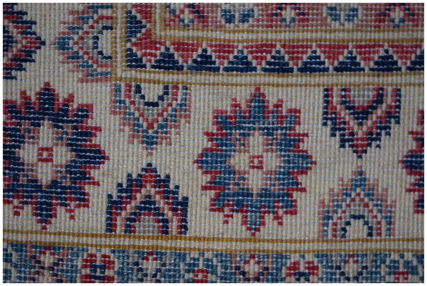 A close-up of an Afghan Kazakh rug featuring traditional geometric motifs in red, blue, and cream.