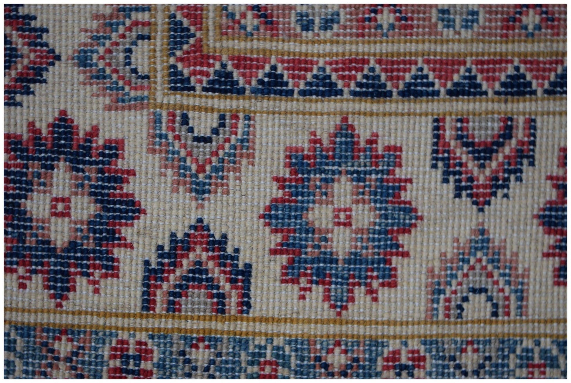 A close-up of an Afghan Kazakh rug featuring traditional geometric motifs in red, blue, and cream.