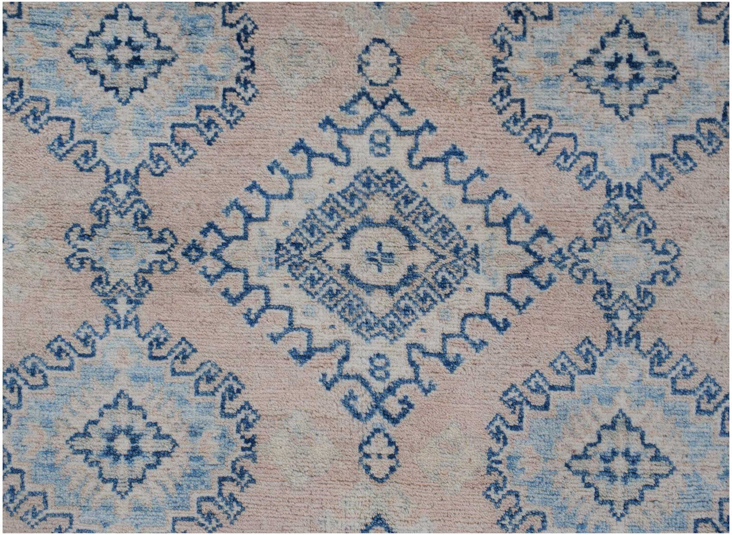 Handmade Afghan Kazakh rug featuring a blue geometric diamond pattern on a soft pink background.