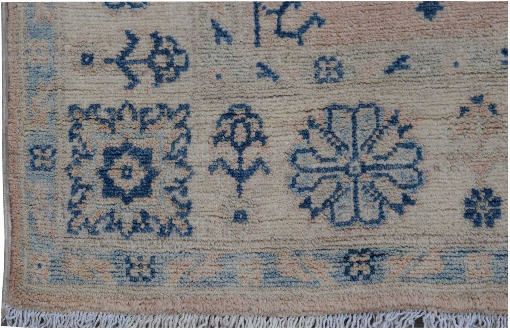 Handmade Afghan Kazakh rug featuring blue geometric and floral motifs on a beige wool background.