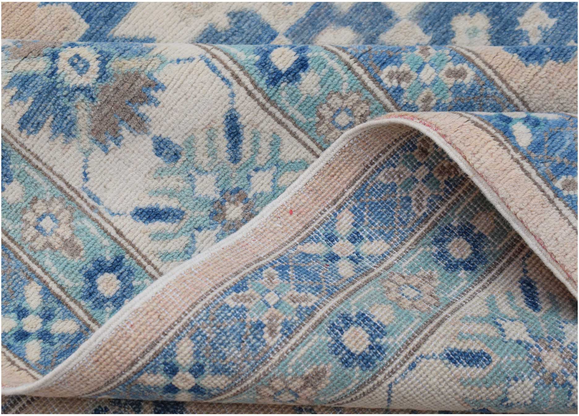 A handmade Afghan Kazakh rug featuring a floral pattern in shades of blue, beige, and grey.