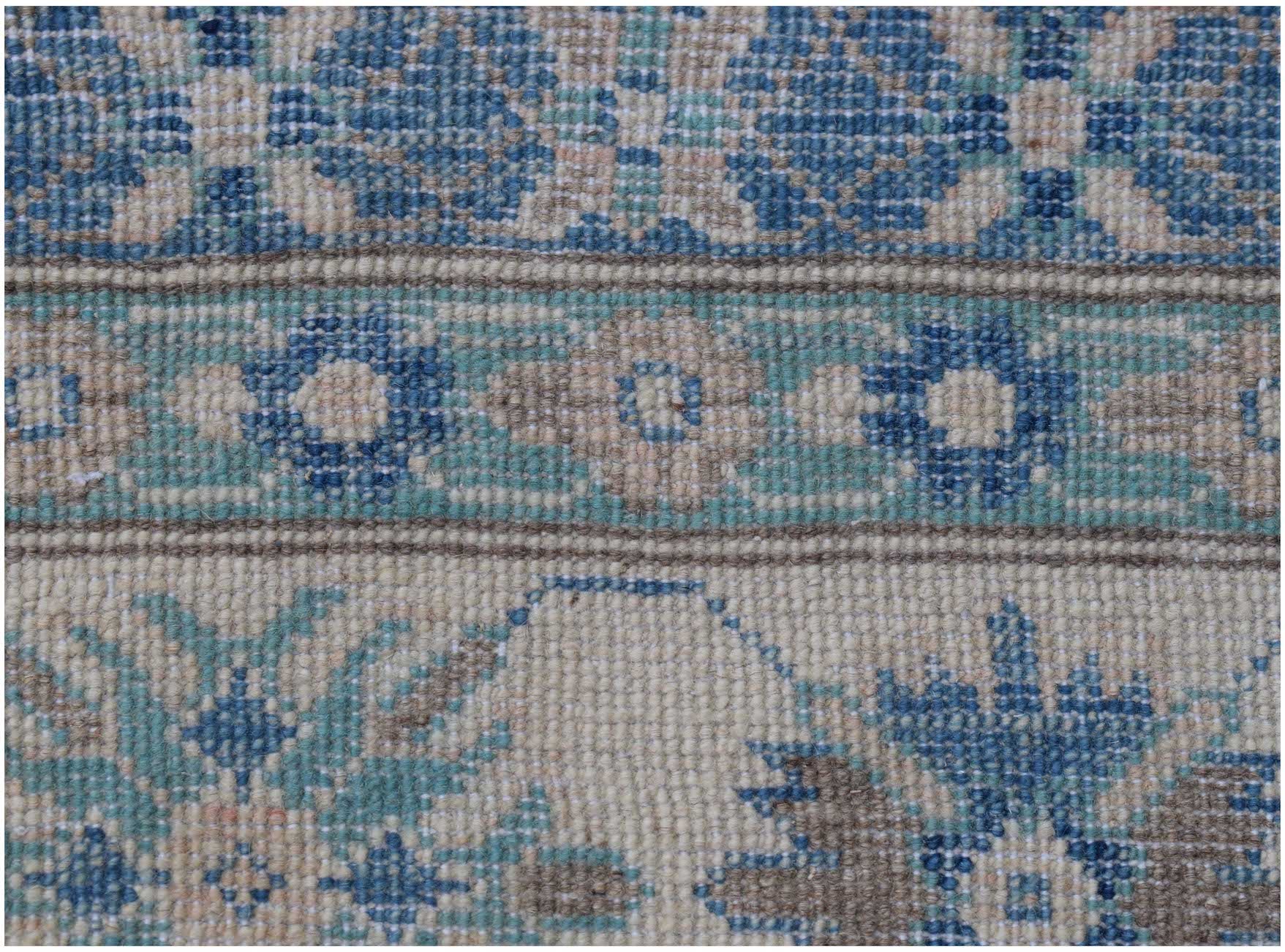A close-up of an Afghan Kazakh rug featuring intricate floral patterns in blue, beige, and grey.