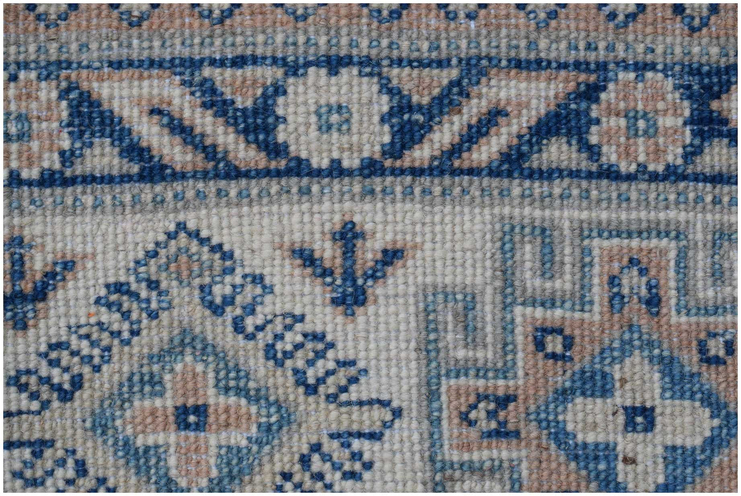 A close-up of a handmade Afghan Kazakh rug featuring geometric blue and beige patterns.