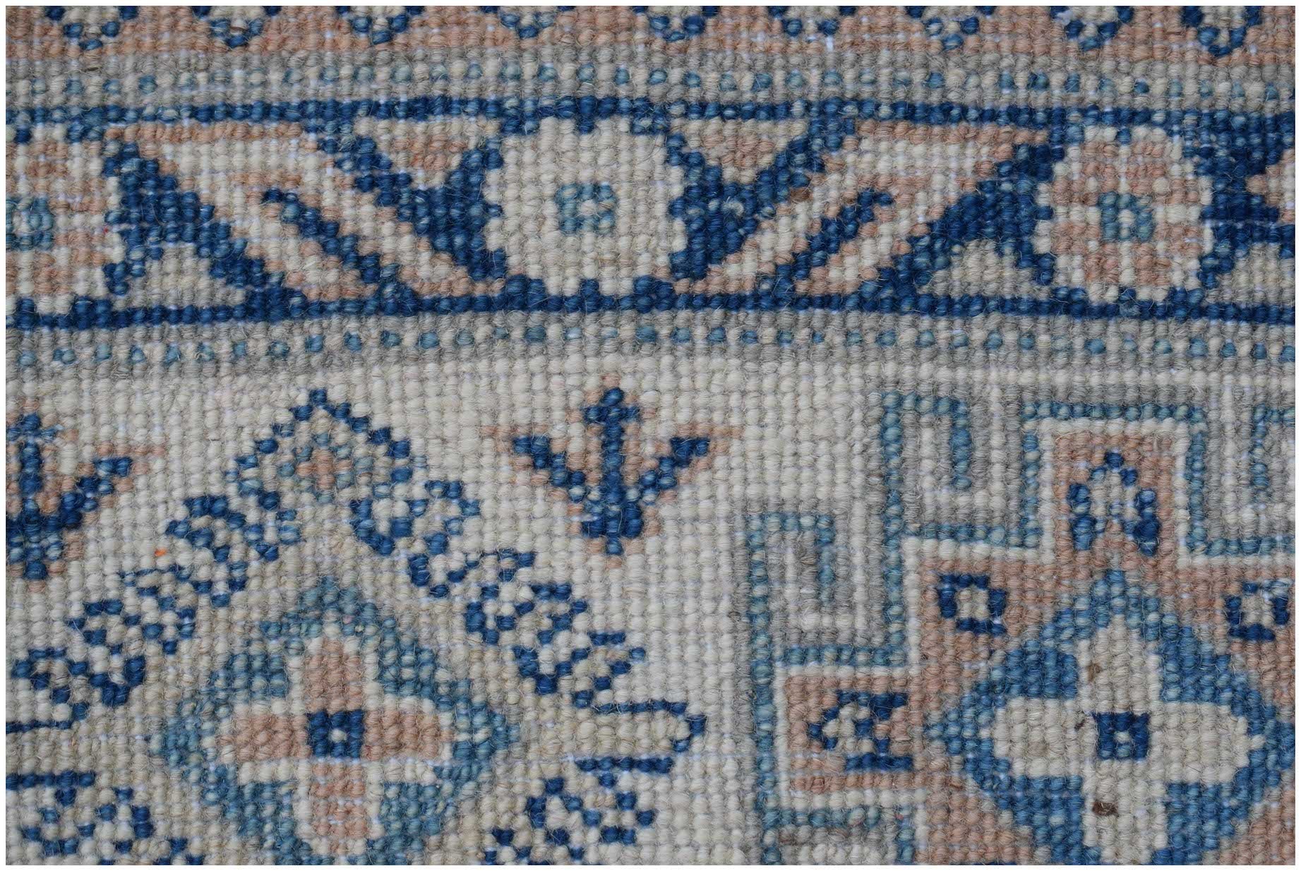 A close-up of a handmade Afghan Kazakh rug featuring geometric blue and beige patterns.