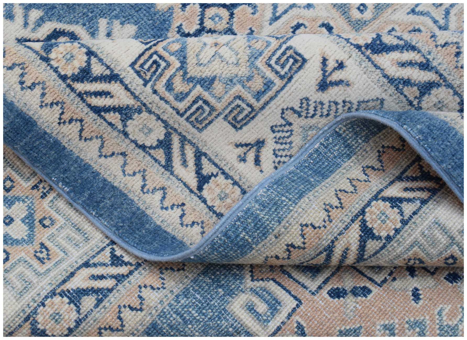 A folded Afghan Kazakh rug featuring a traditional geometric pattern in shades of blue and beige.