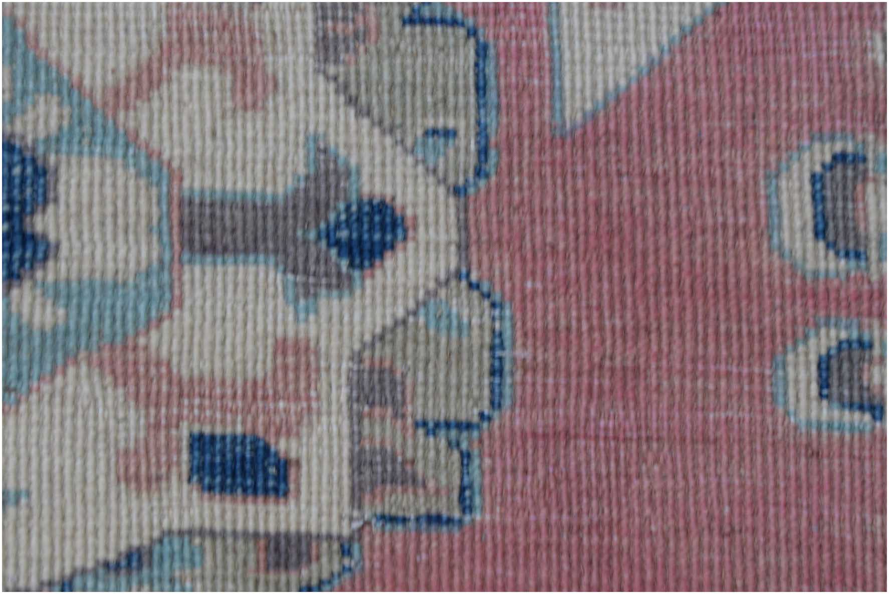 A close-up view of a handmade Afghan Kazakh rug featuring traditional motifs in pink, blue, and tan.