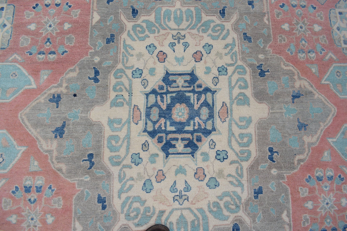 Handmade Afghan Kazakh rug featuring a geometric central medallion in blue, pink, and grey tones.