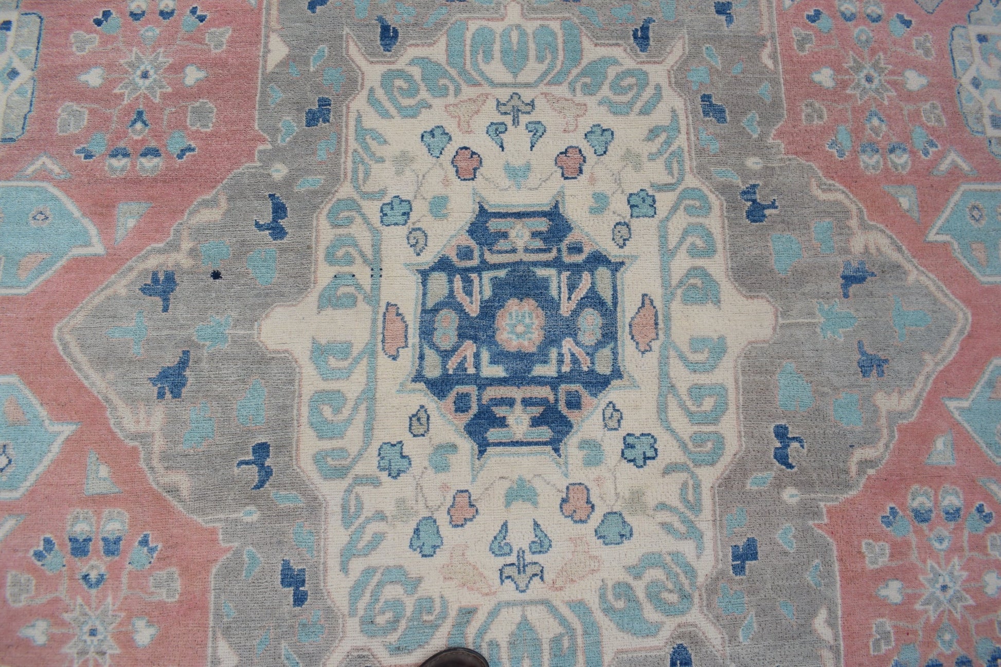 Handmade Afghan Kazakh rug featuring a geometric central medallion in blue, pink, and grey tones.