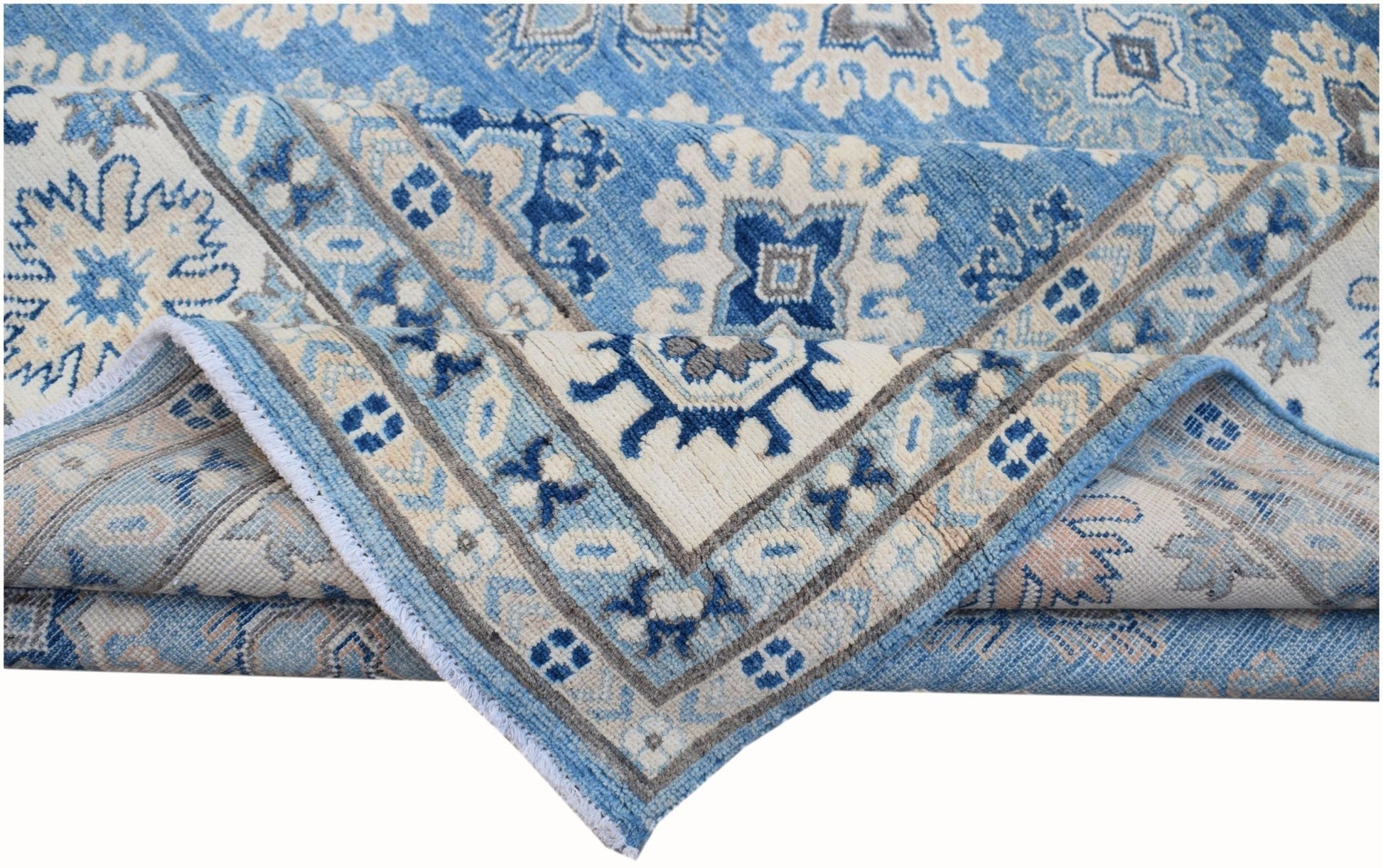 A folded Afghan Kazakh rug featuring a geometric pattern in shades of blue, beige, and grey.