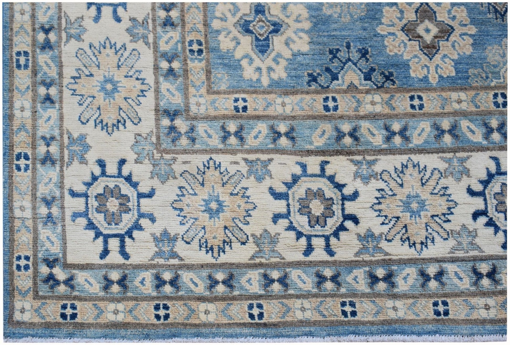 An Afghan Kazakh rug featuring a geometric floral pattern in shades of blue, beige, and grey.