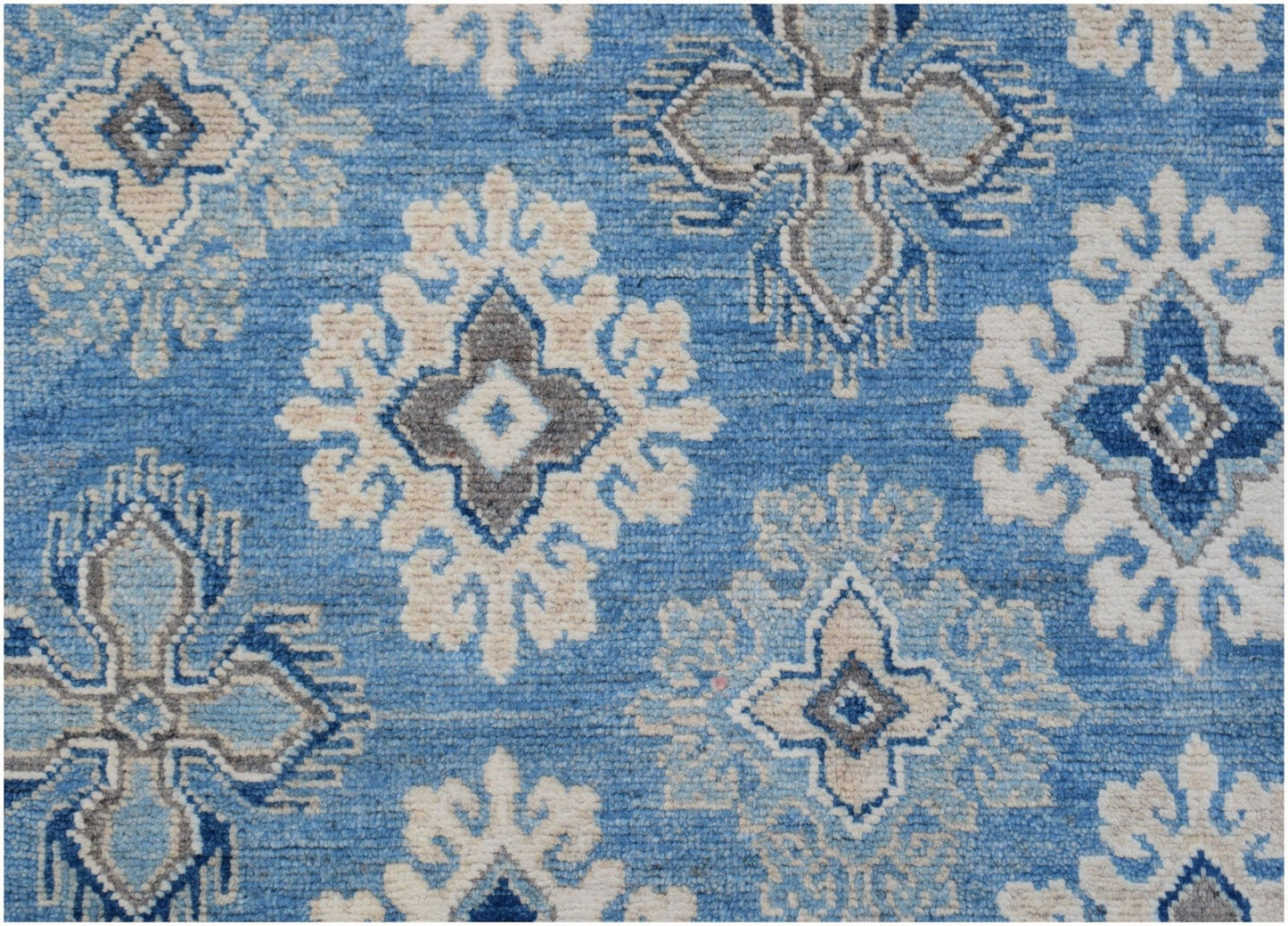 Handmade Afghan Kazakh rug featuring a repeating geometric floral pattern in blue, grey, and beige.