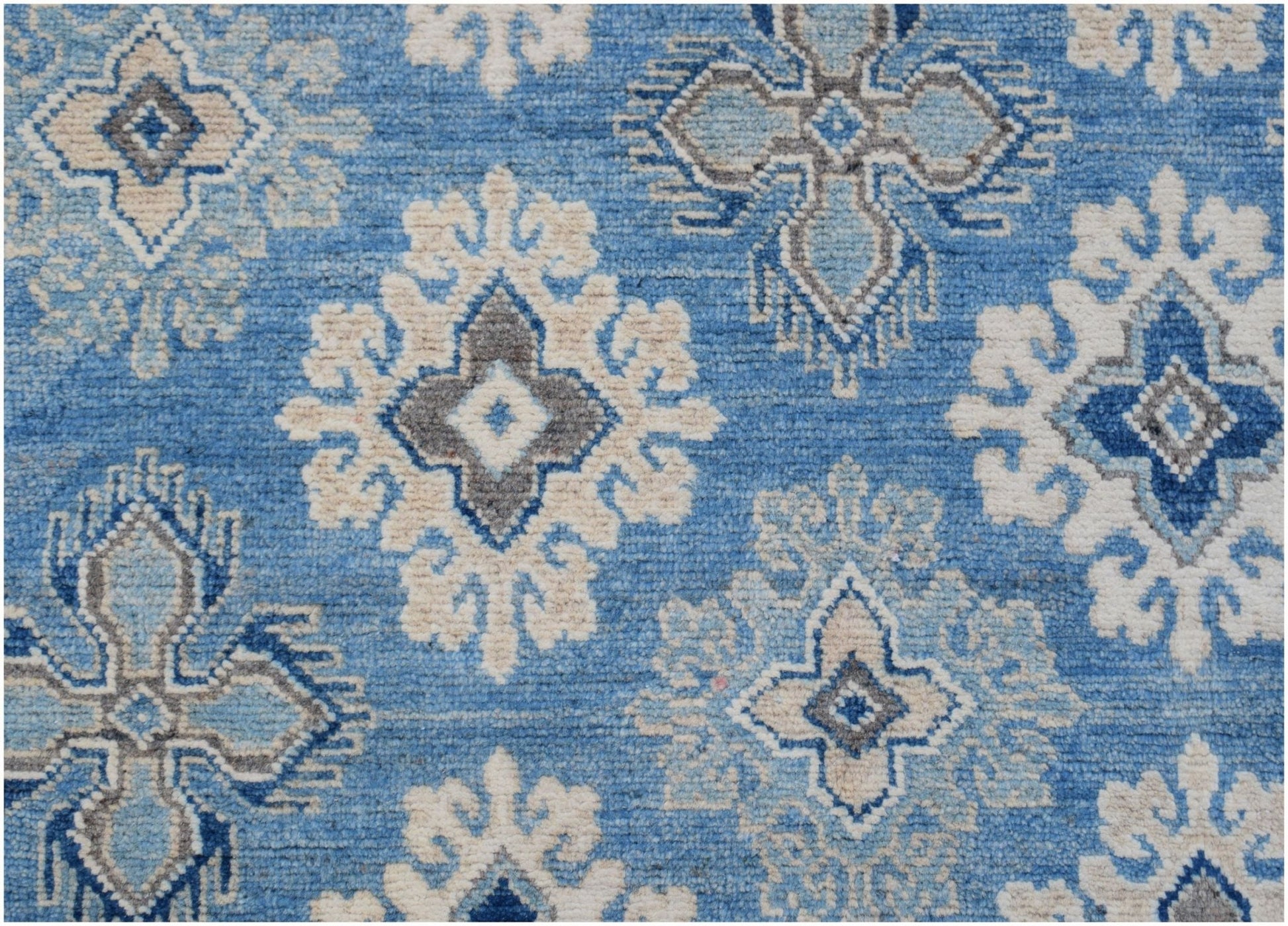 Handmade Afghan Kazakh rug featuring a repeating geometric floral pattern in blue, grey, and beige.