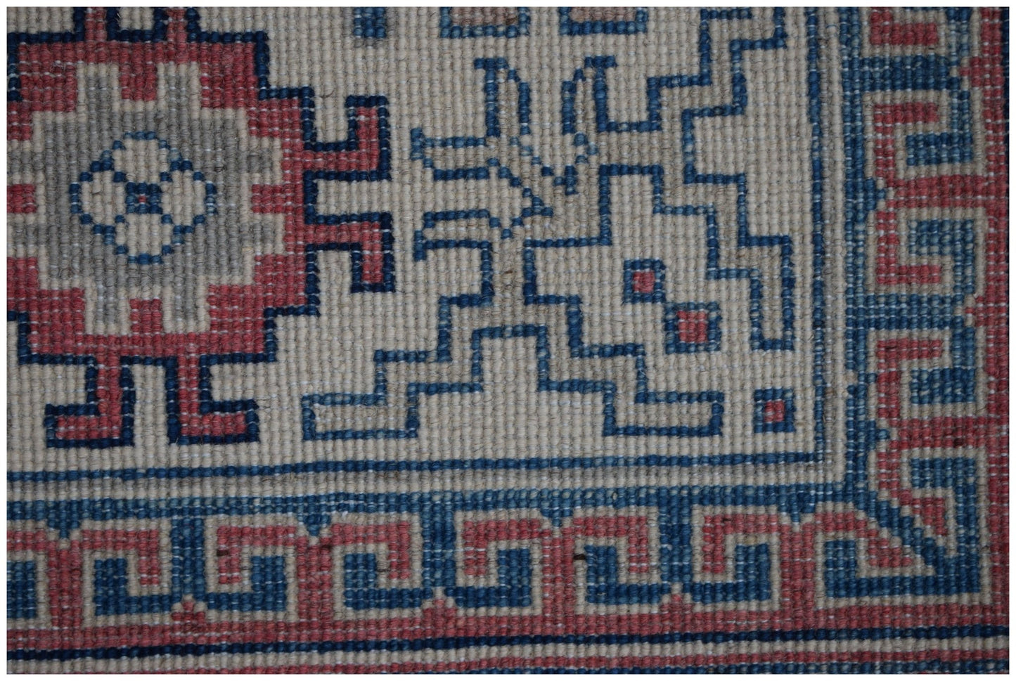 A close-up of a handmade Afghan Kazakh rug featuring geometric red and blue patterns on a cream base.