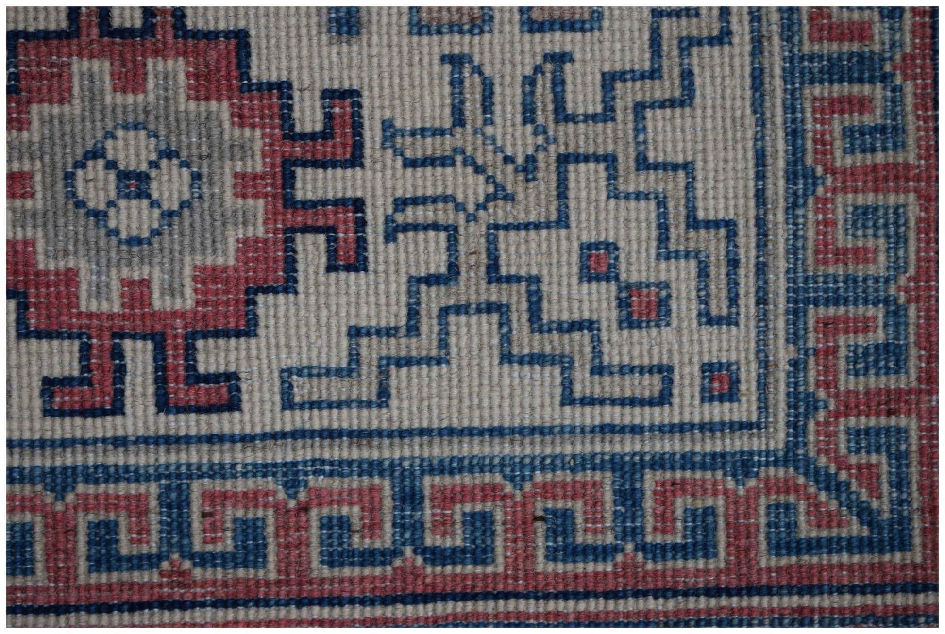 A close-up of a handmade Afghan Kazakh rug featuring geometric red and blue patterns on a cream base.