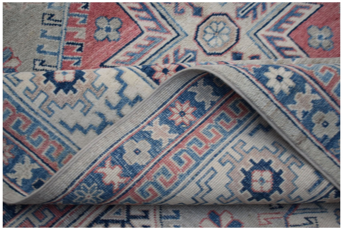 A handmade Afghan Kazakh rug featuring traditional geometric patterns in blue, pink, and cream.