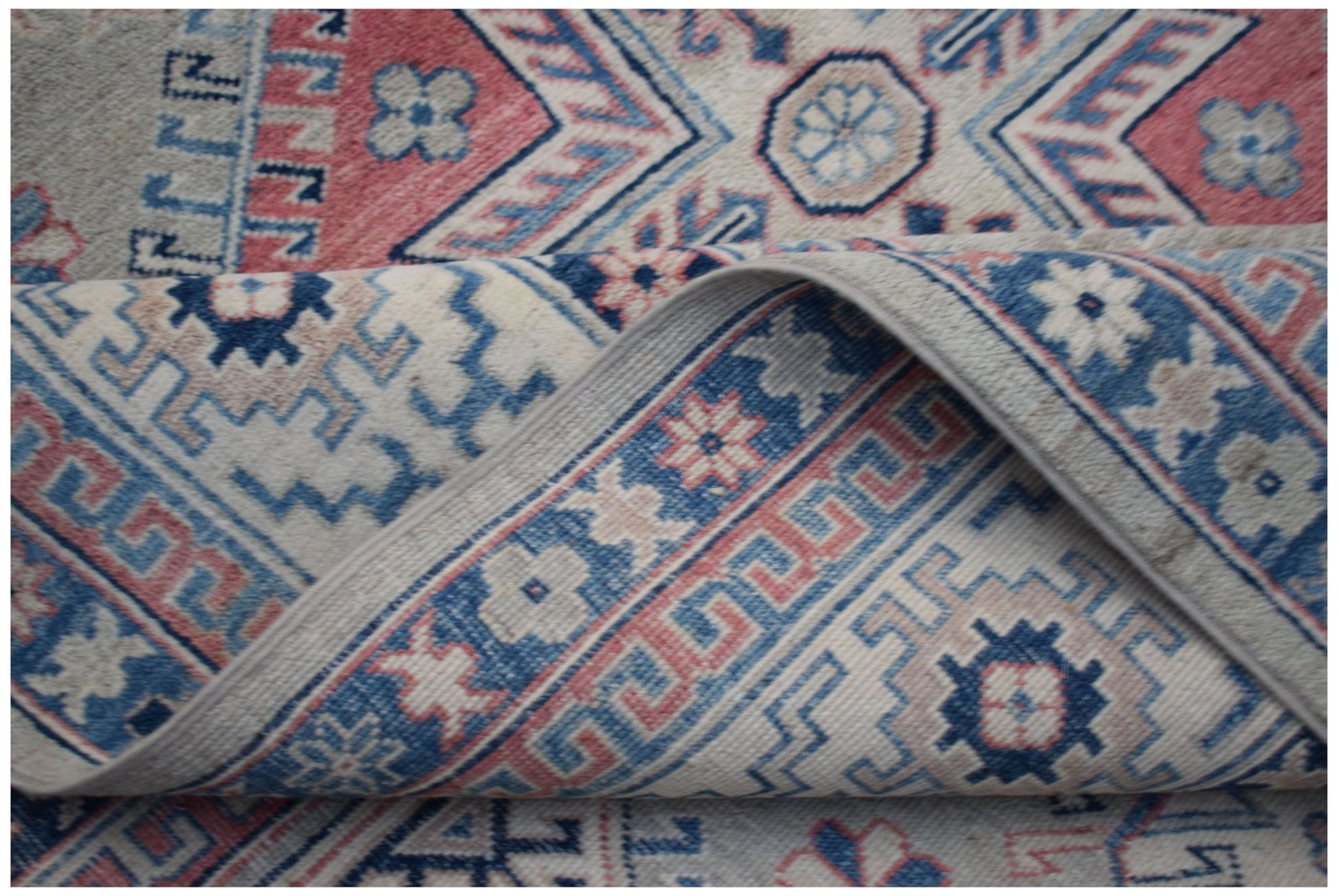 A handmade Afghan Kazakh rug featuring traditional geometric patterns in blue, pink, and cream.