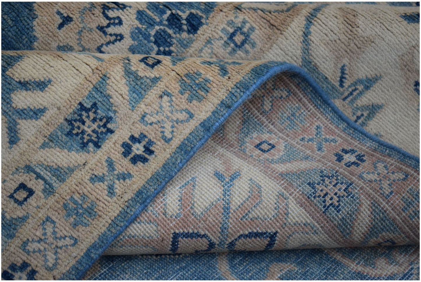 A folded Afghan Kazakh wool rug featuring traditional geometric patterns in blue and beige.