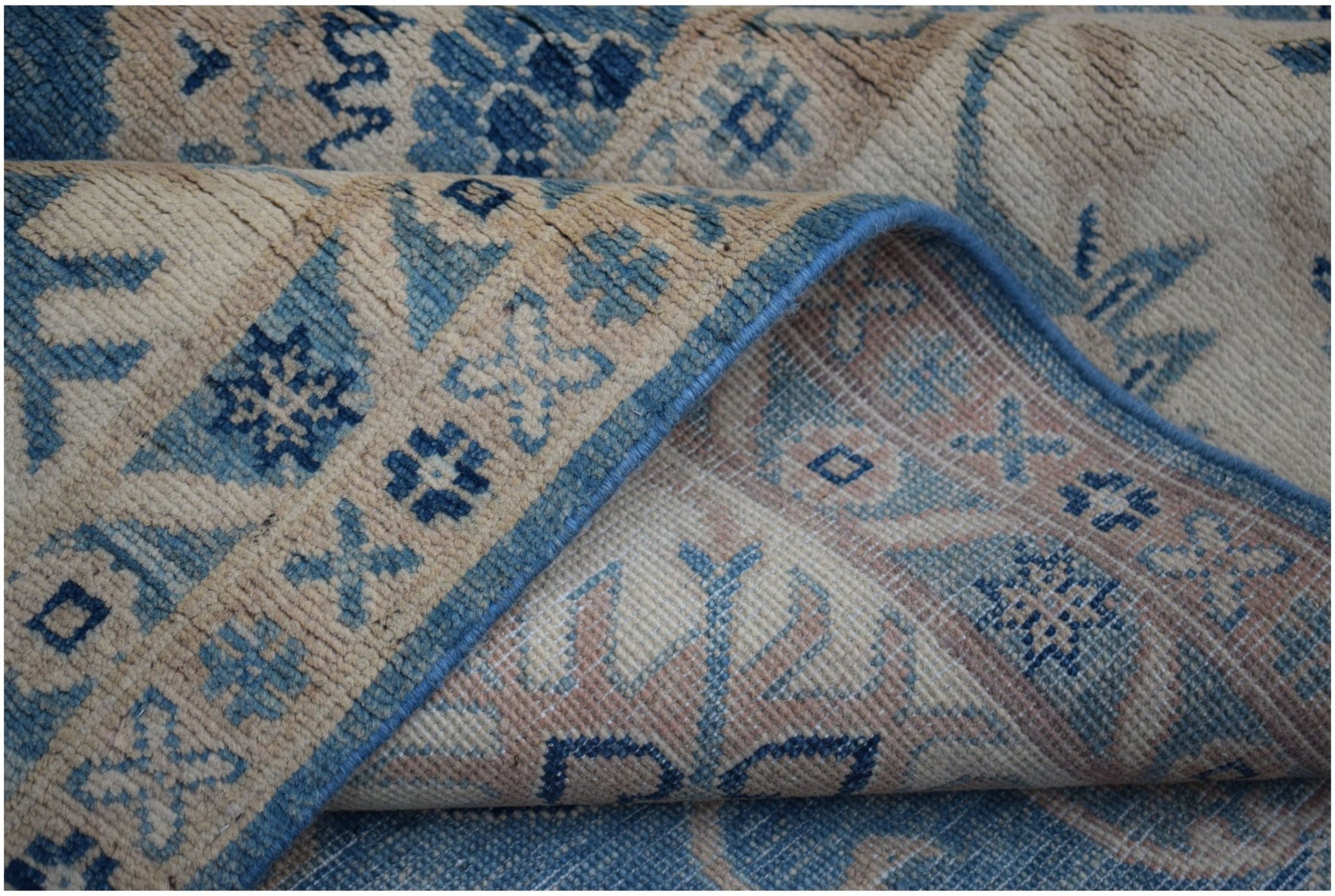 A folded Afghan Kazakh wool rug featuring traditional geometric patterns in blue and beige.