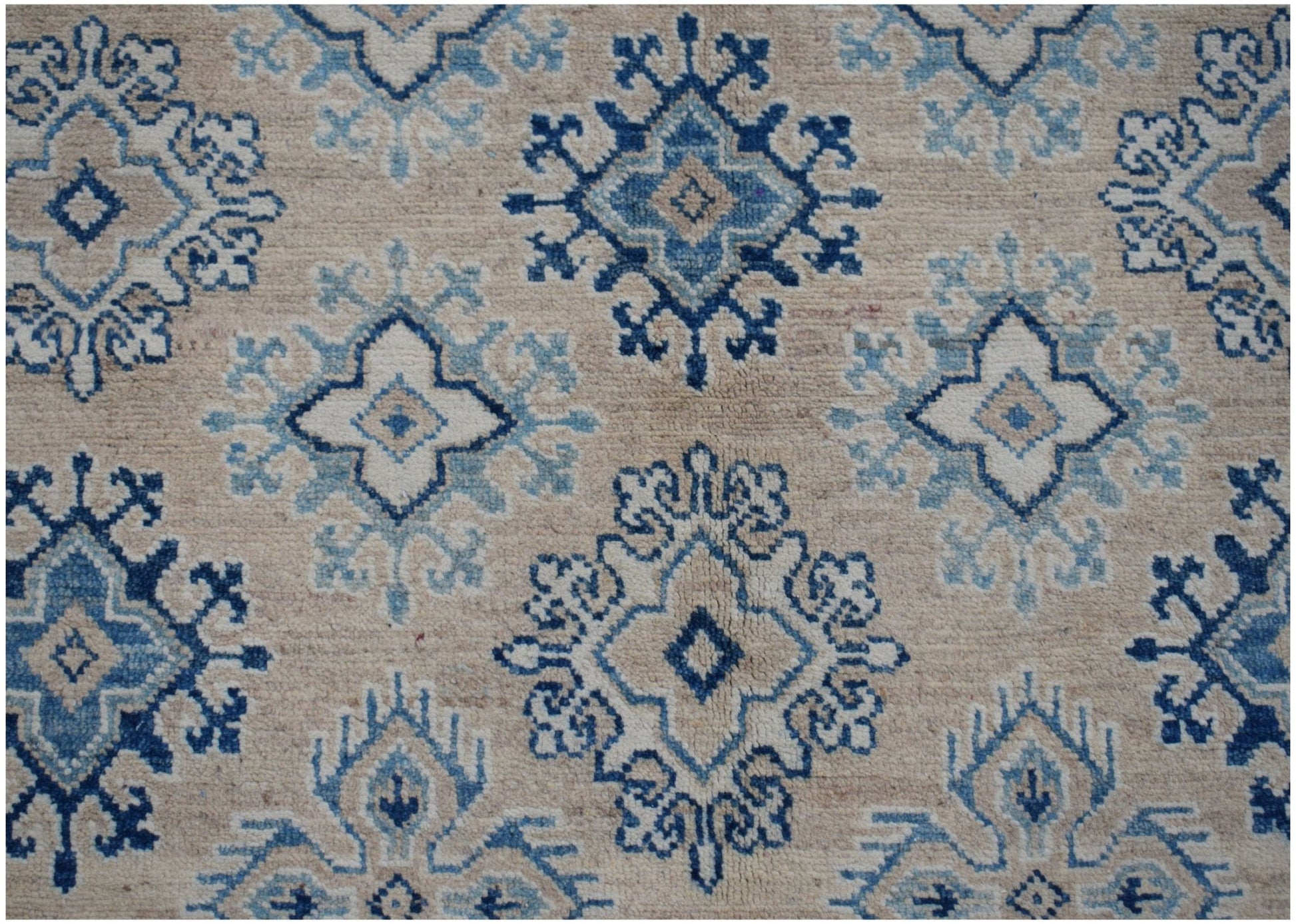 Handmade Afghan Kazakh rug featuring a repeating geometric floral pattern in blue and beige tones.