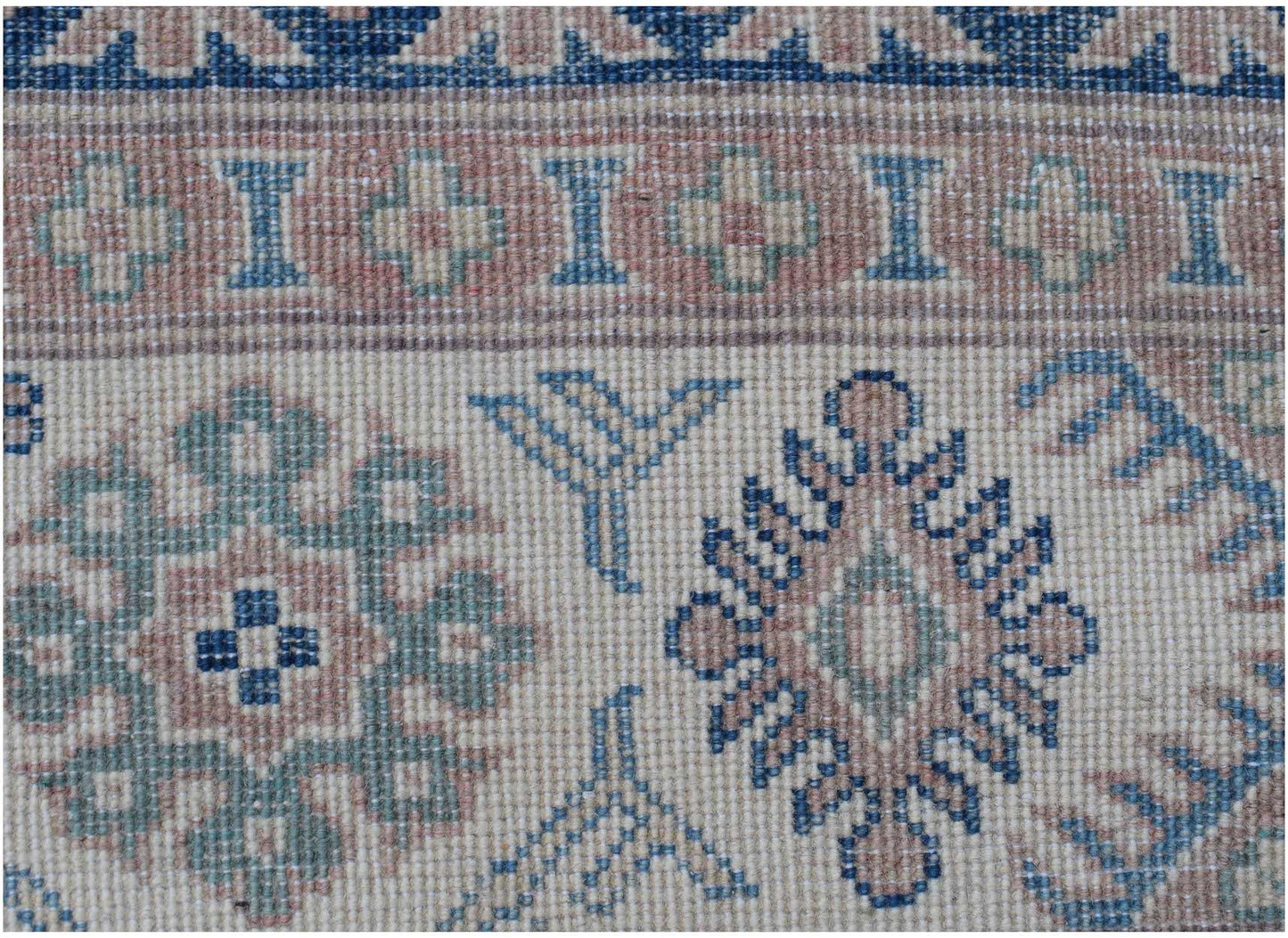A close-up of an Afghan Kazakh rug featuring traditional geometric motifs in blue and tan wool.