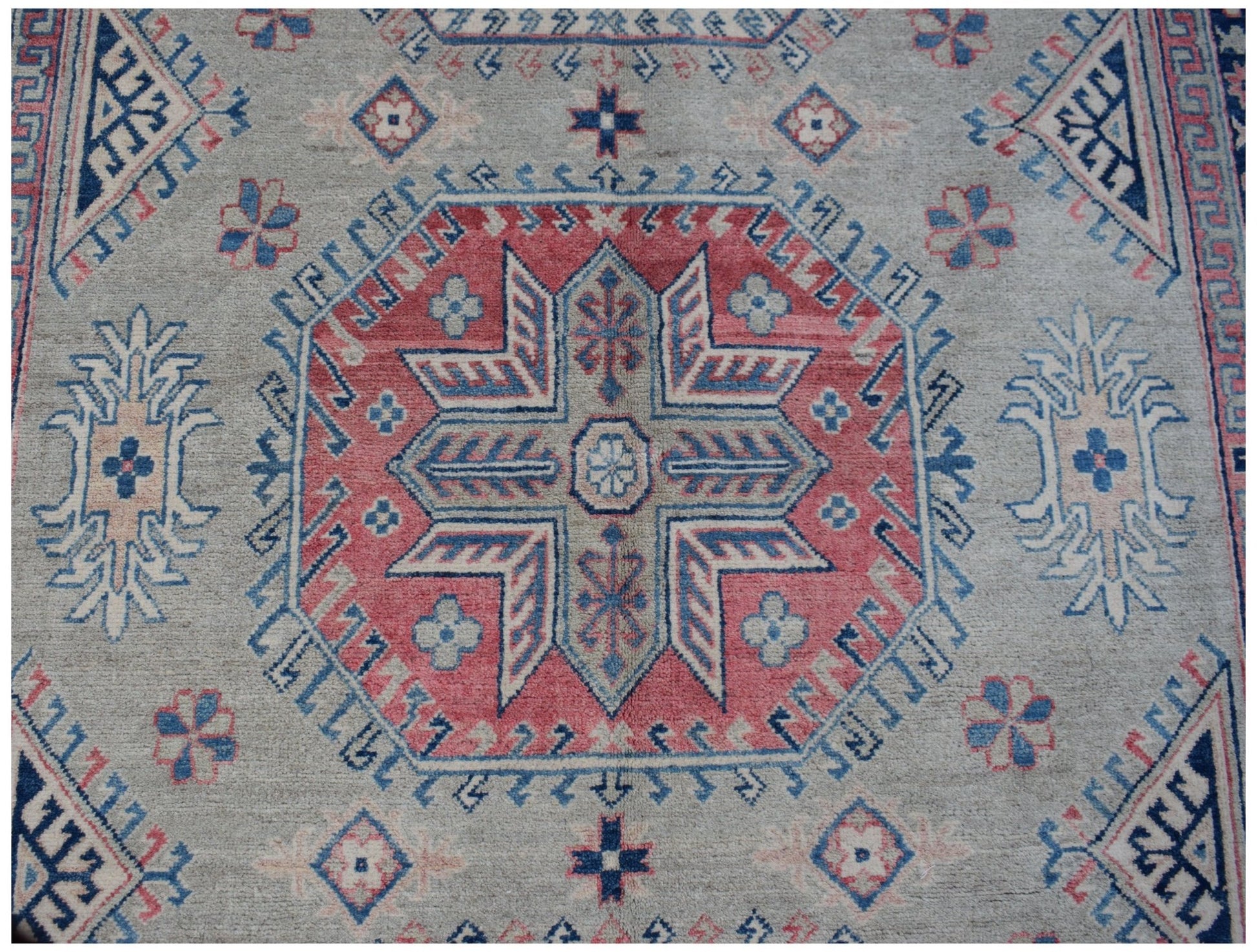 Handmade Afghan Kazakh rug featuring a central geometric medallion in red, blue, and cream wool.
