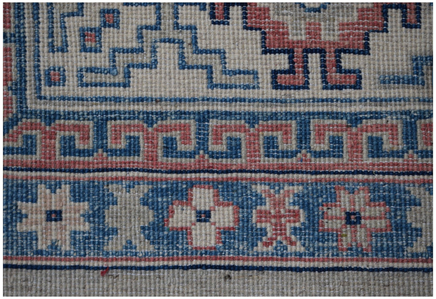 A close-up of an Afghan Kazakh rug featuring geometric patterns in blue, red, and cream wool.
