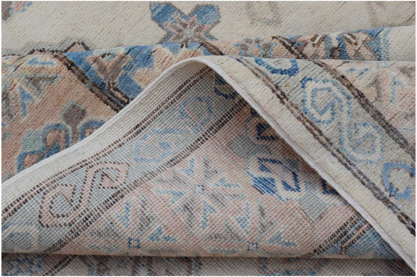 A corner of a handmade Afghan Kazakh wool rug with a traditional pattern in blue and soft pink.