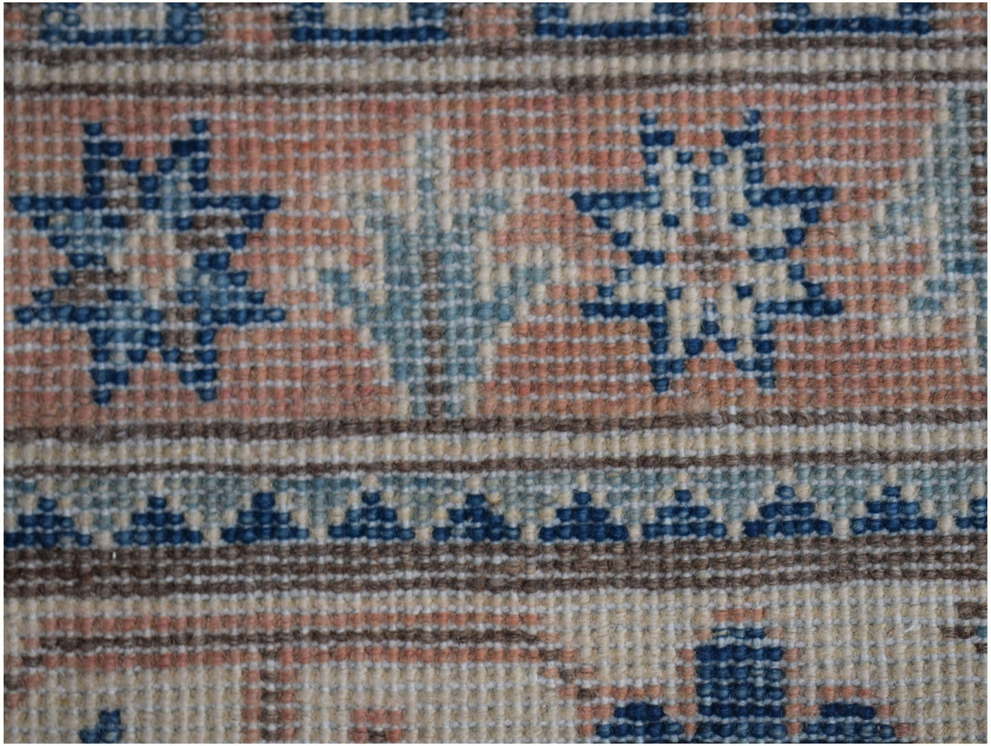 A close-up of a handmade Afghan Kazakh rug featuring geometric star and floral patterns in blue.