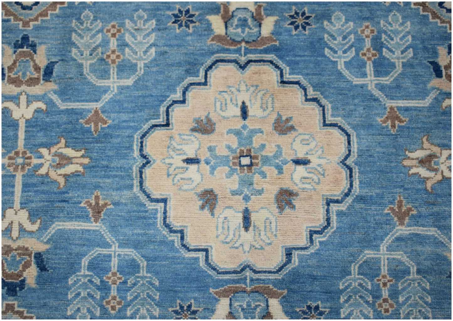 An Afghan Kazakh rug featuring a central beige medallion with blue and grey floral motifs.