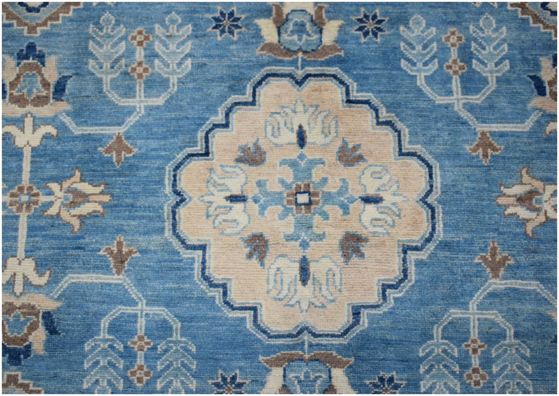 An Afghan Kazakh rug featuring a central beige medallion with blue and grey floral motifs.