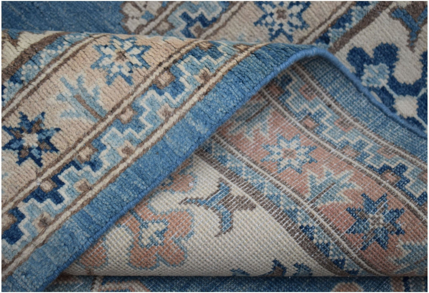 A folded Afghan Kazakh rug featuring a geometric floral pattern in shades of blue, beige, and pink.