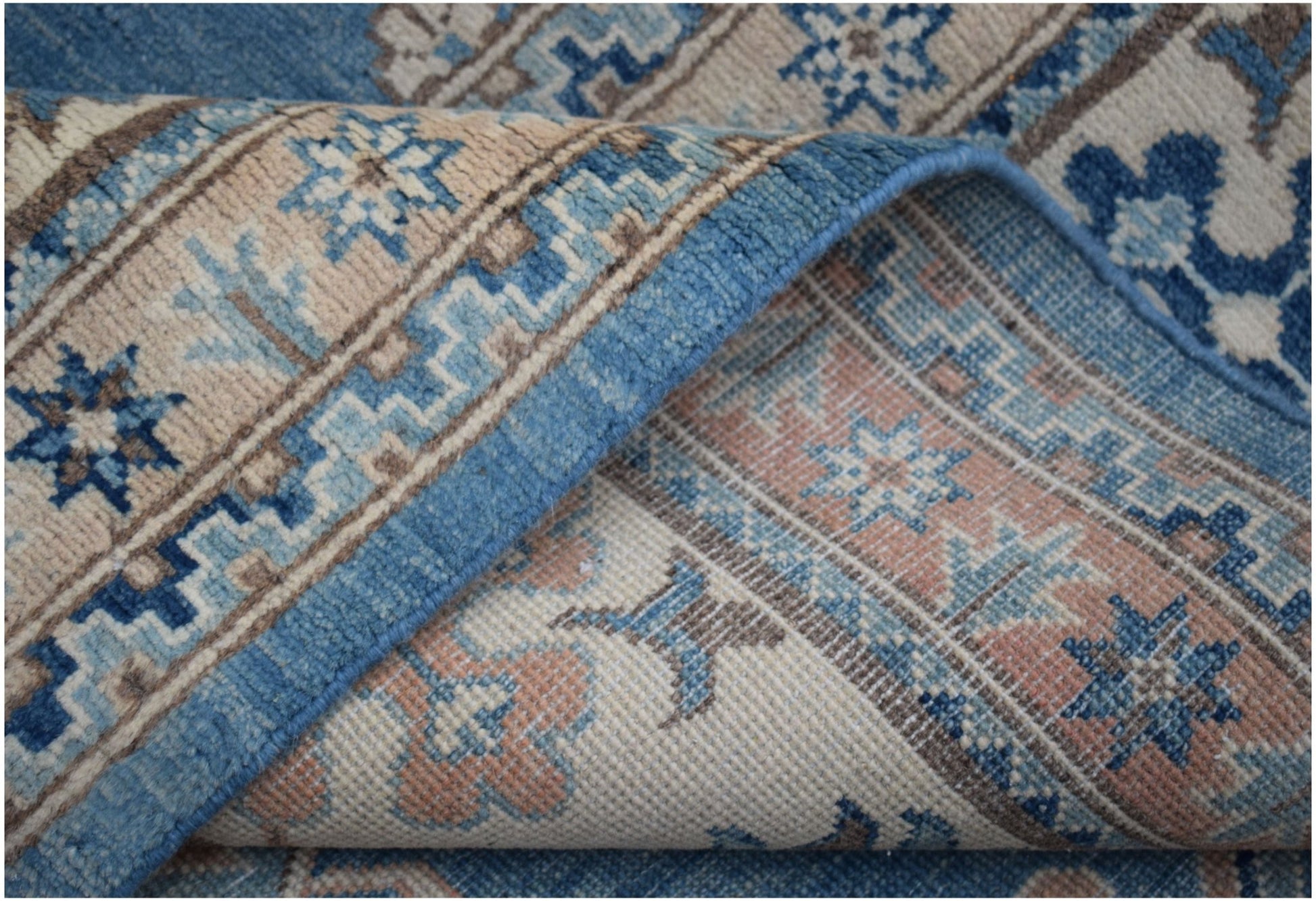 A folded Afghan Kazakh rug featuring a geometric floral pattern in shades of blue, beige, and pink.