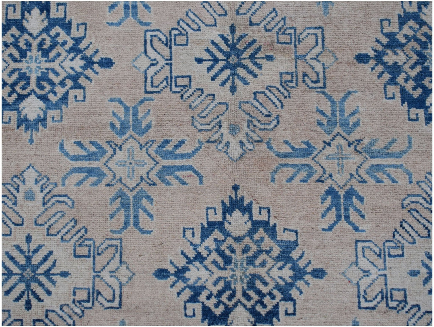 Handmade Afghan Kazakh rug featuring a repeating blue geometric snowflake pattern on a beige field.