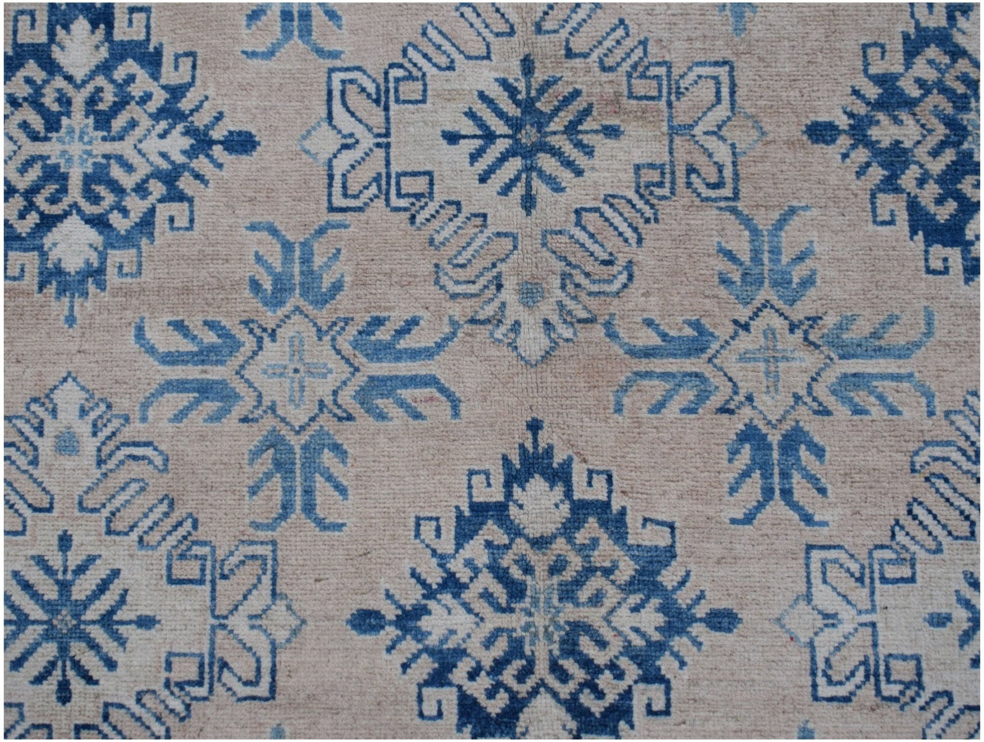 Handmade Afghan Kazakh rug featuring a repeating blue geometric snowflake pattern on a beige field.