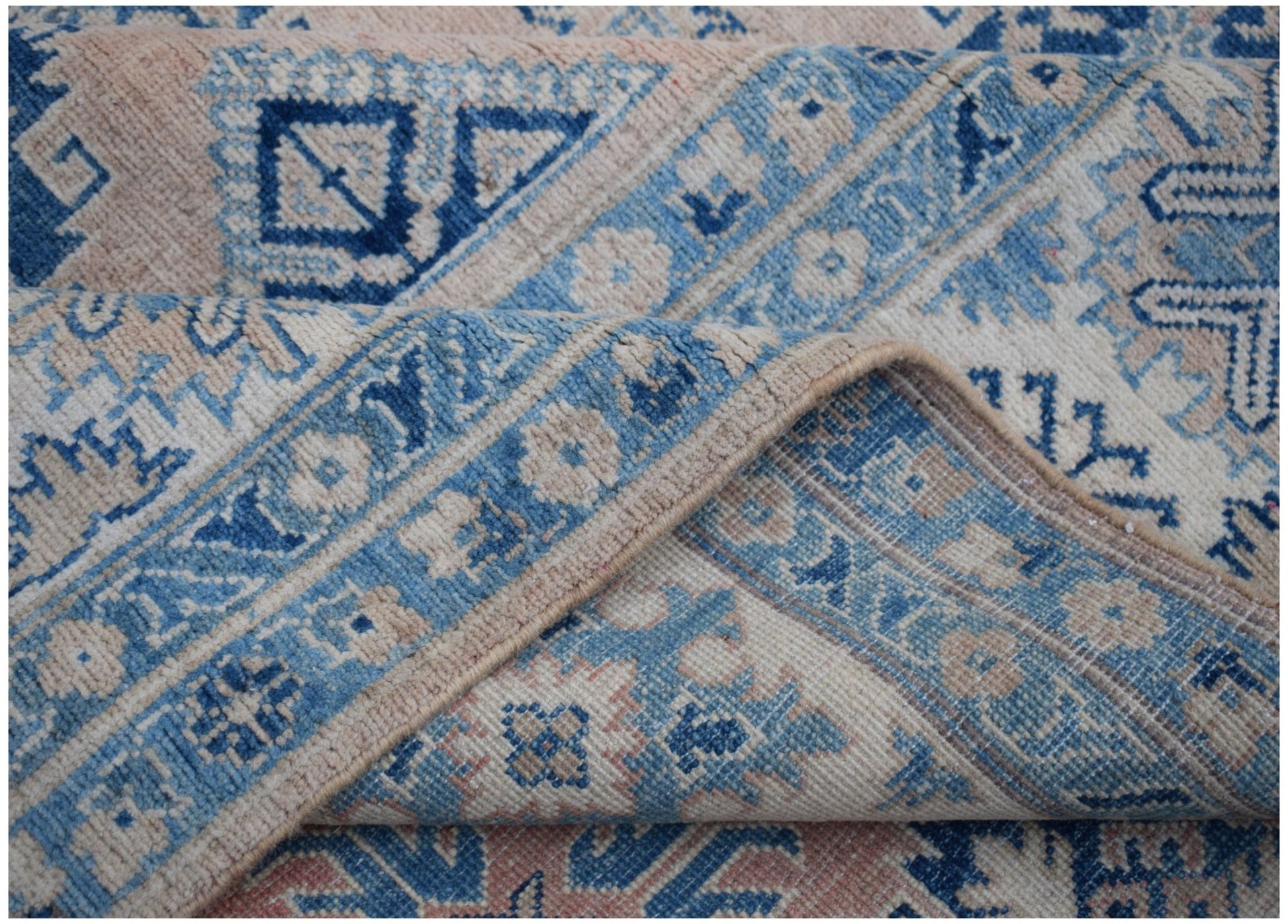 A handmade Afghan Kazakh rug featuring traditional geometric patterns in blue, cream, and pink.