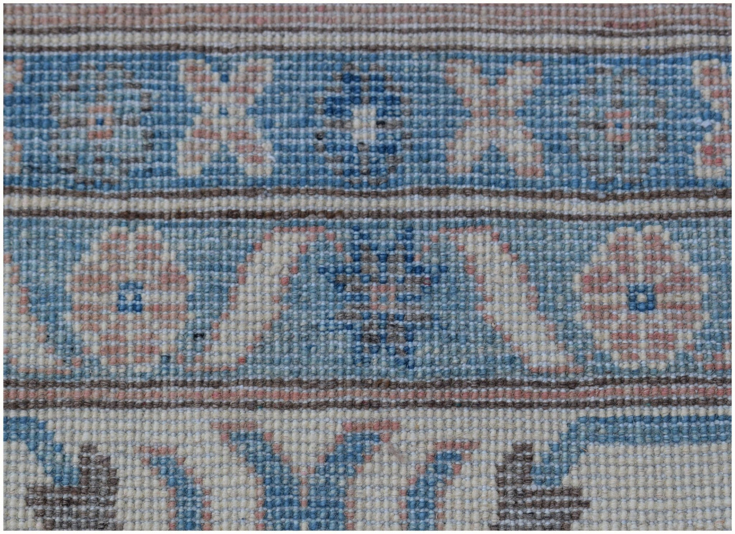 A close-up of a handmade Afghan Kazakh rug featuring geometric floral patterns in blue and pink.