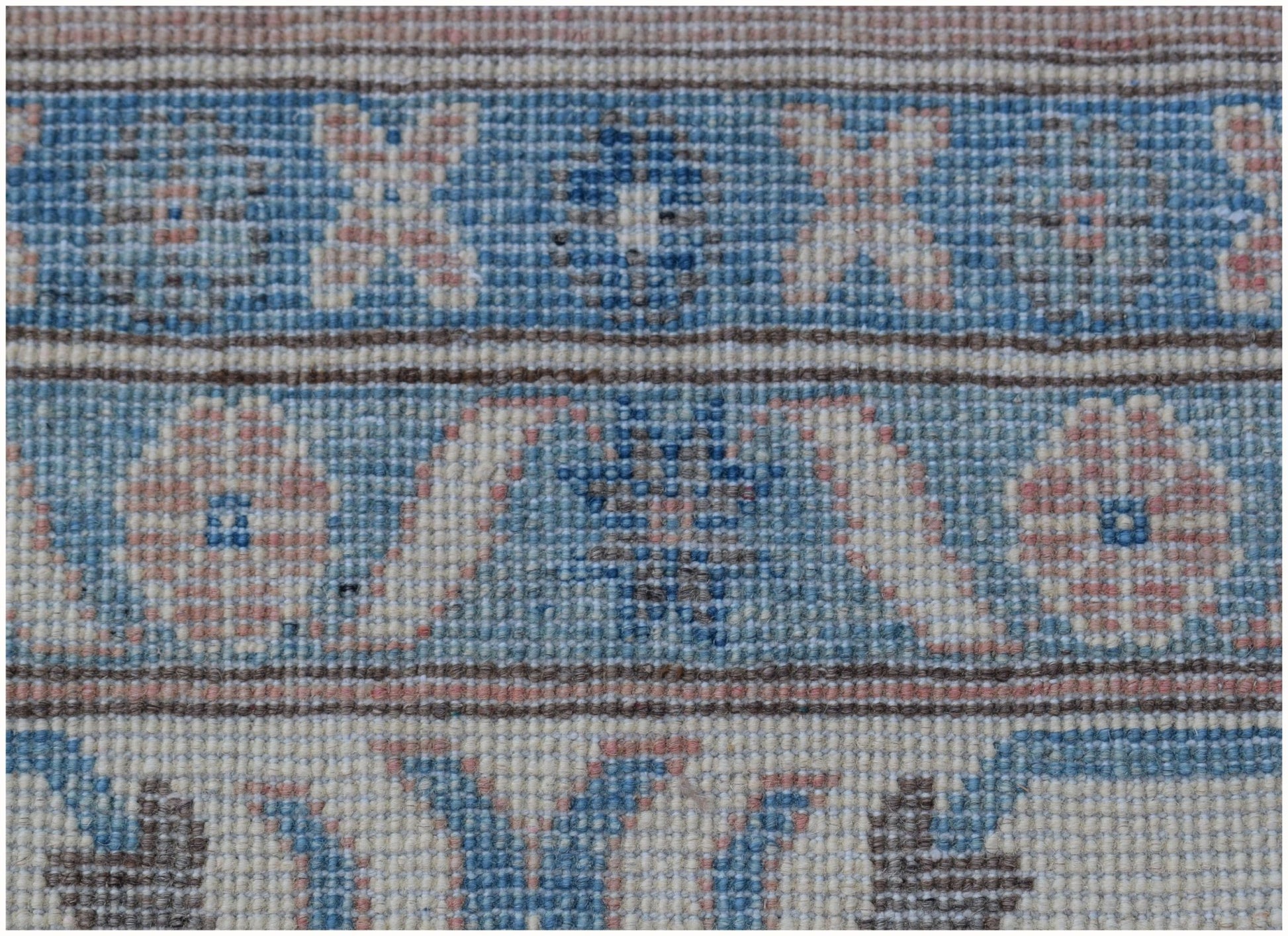A close-up of a handmade Afghan Kazakh rug featuring geometric floral patterns in blue and pink.