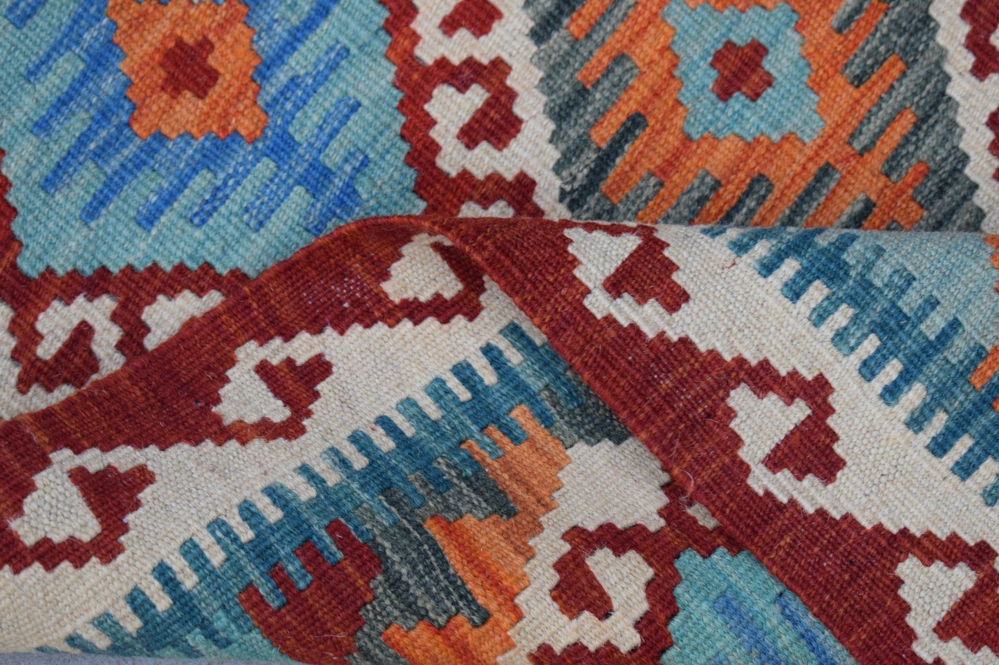 A folded Afghan Maimana kilim rug featuring a geometric pattern in red, blue, and orange wool.