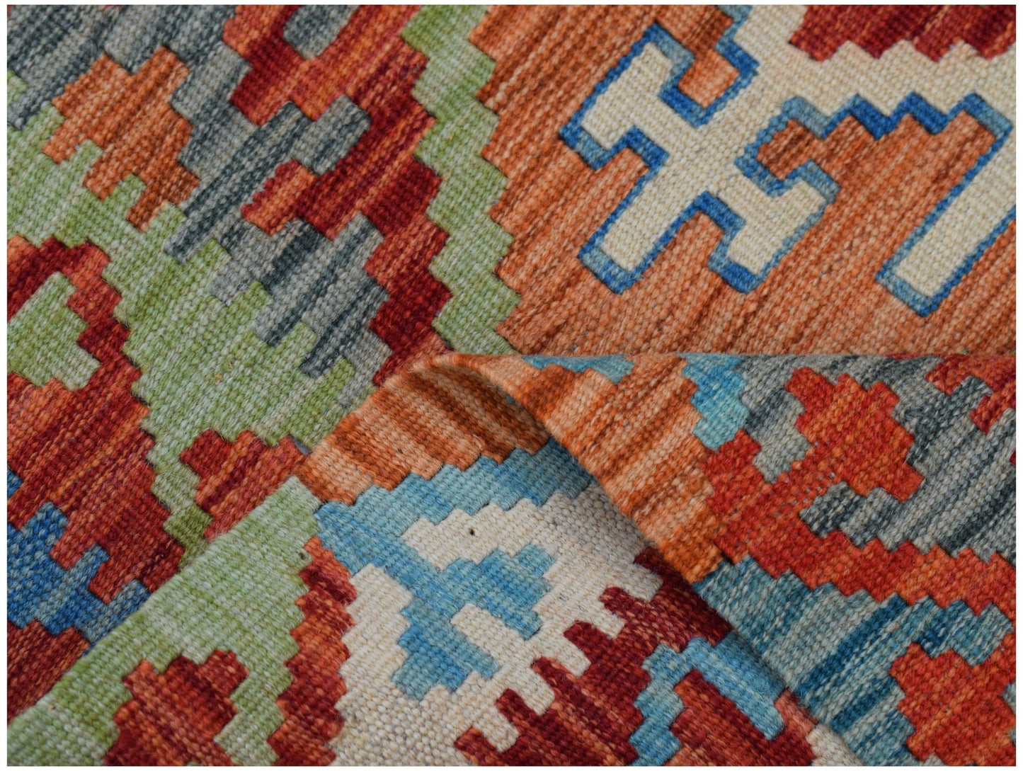 A handmade Afghan Maimana kilim rug featuring a geometric pattern in vibrant red, blue, and green.