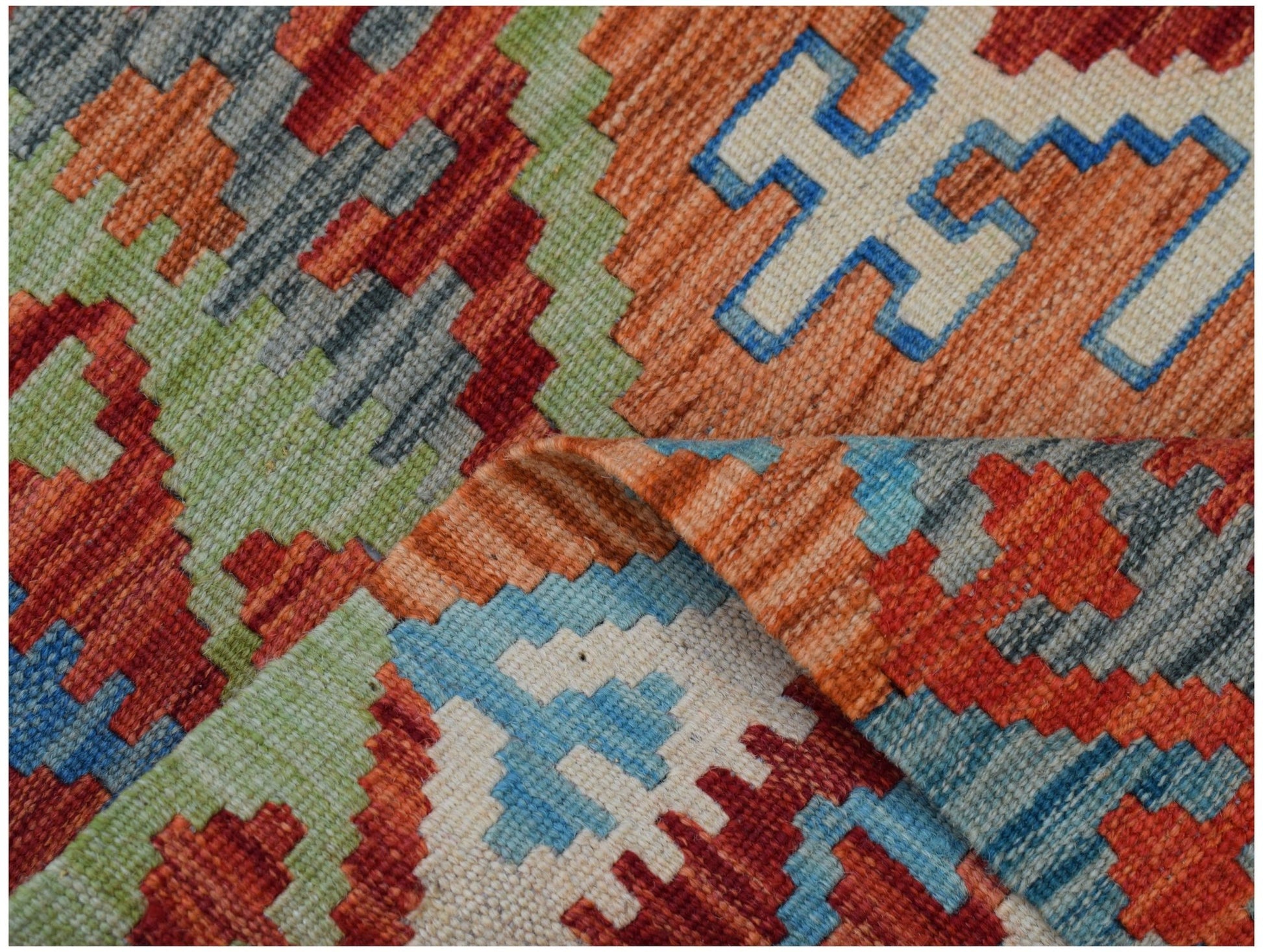 A handmade Afghan Maimana kilim rug featuring a geometric pattern in vibrant red, blue, and green.