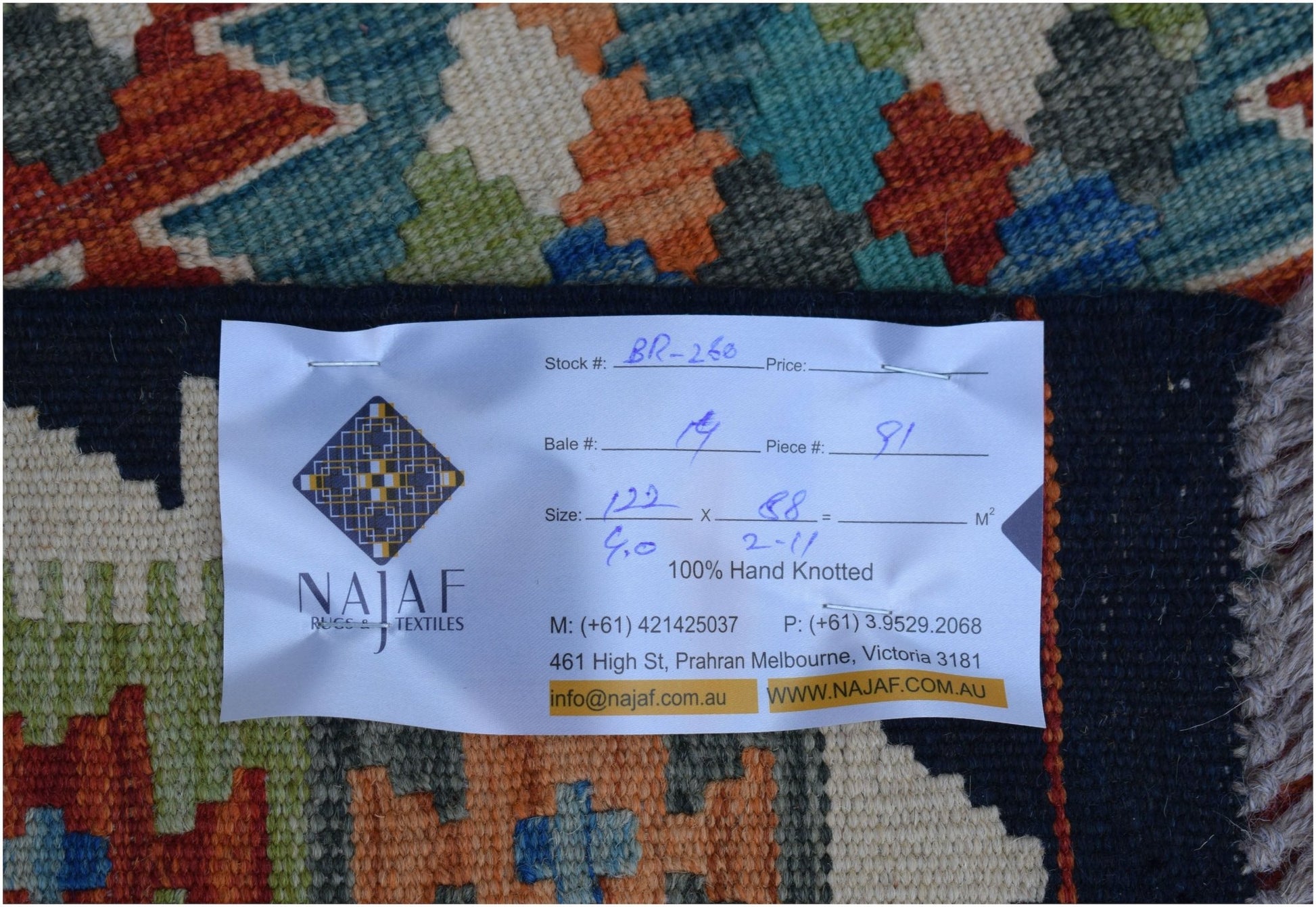 A close-up of an Afghan Maimana Kilim featuring a geometric pattern and a product information tag.