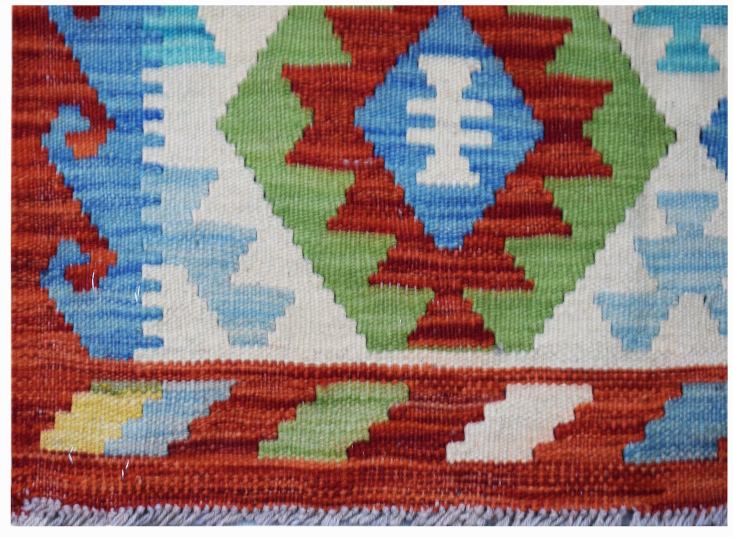 Handwoven Afghan Maimana kilim featuring a geometric pattern in red, blue, green, and cream wool.