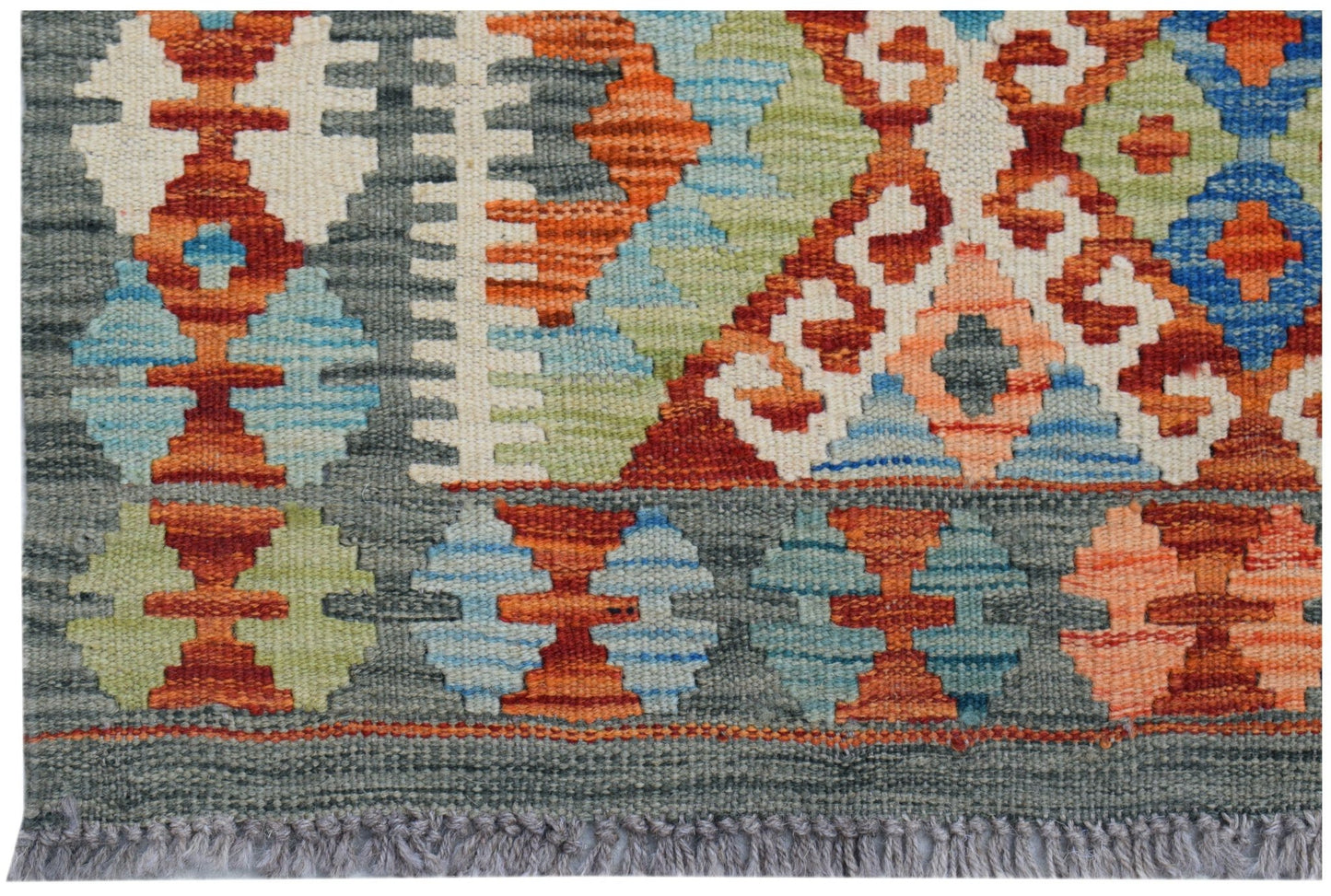 Handwoven Afghan Maimana kilim rug featuring a colorful geometric pattern on a grey background.