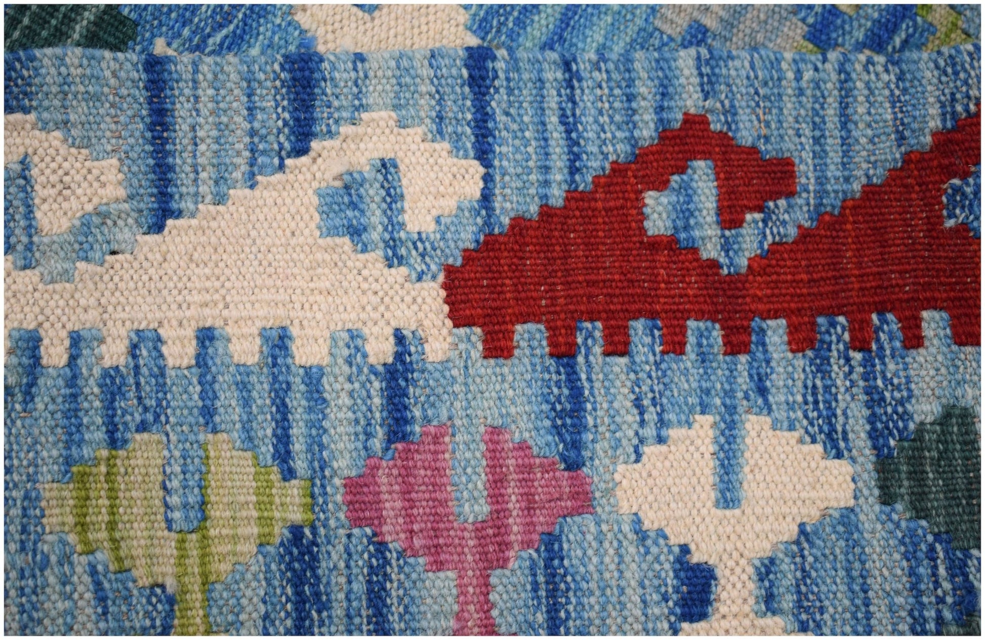 A handmade Afghan Maimana kilim featuring geometric patterns in red, white, pink, and green.