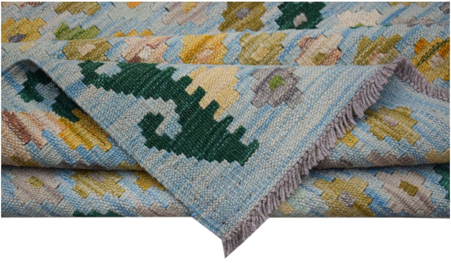 A handmade Afghan Maimana kilim rug featuring a light blue background with geometric floral motifs.