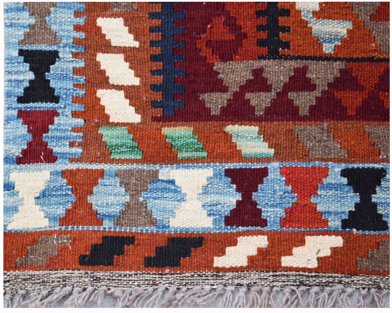 A handwoven Afghan Maimana kilim rug featuring a geometric pattern in vibrant, multi-colored wool.