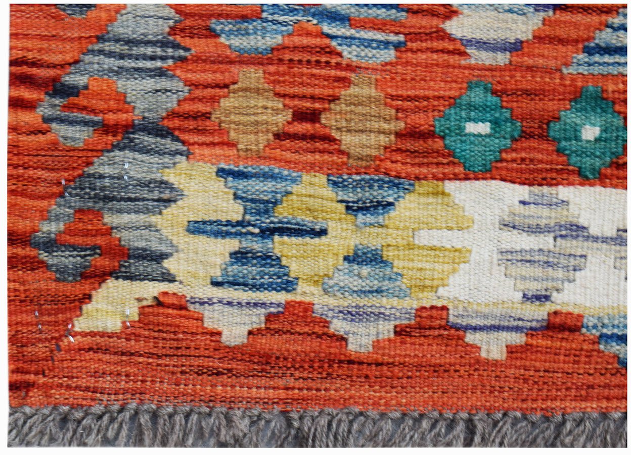 A handwoven Afghan Maimana kilim rug featuring geometric patterns in vibrant orange and blue tones.