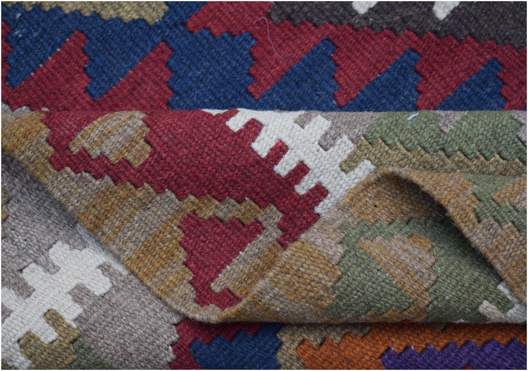 A handwoven Afghan Maimana kilim rug featuring a geometric pattern in rich, multicolored wool.