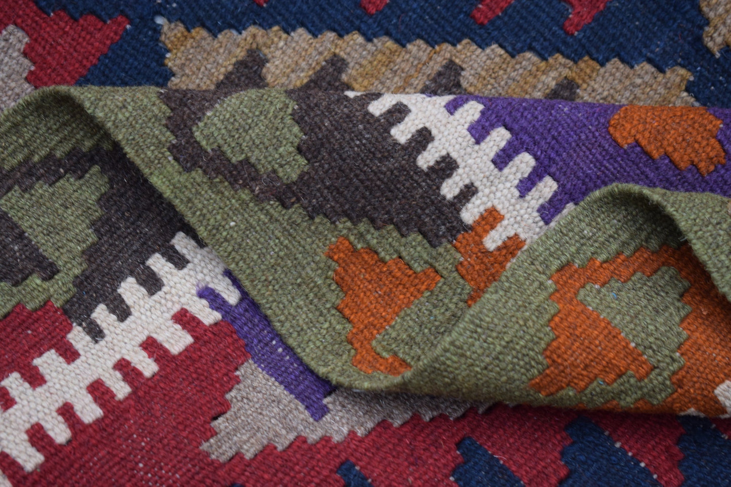 A handmade Afghan Maimana kilim rug featuring a geometric pattern in vibrant wool colors.