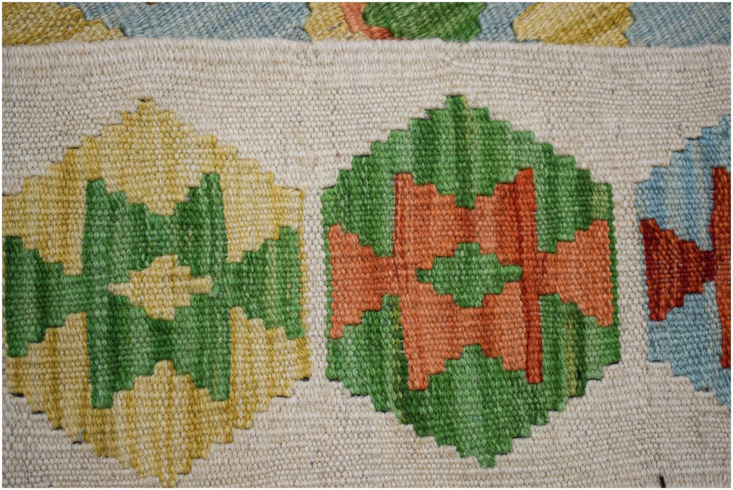 A handmade Afghan Maimana kilim featuring a repeating pattern of colorful geometric shapes.